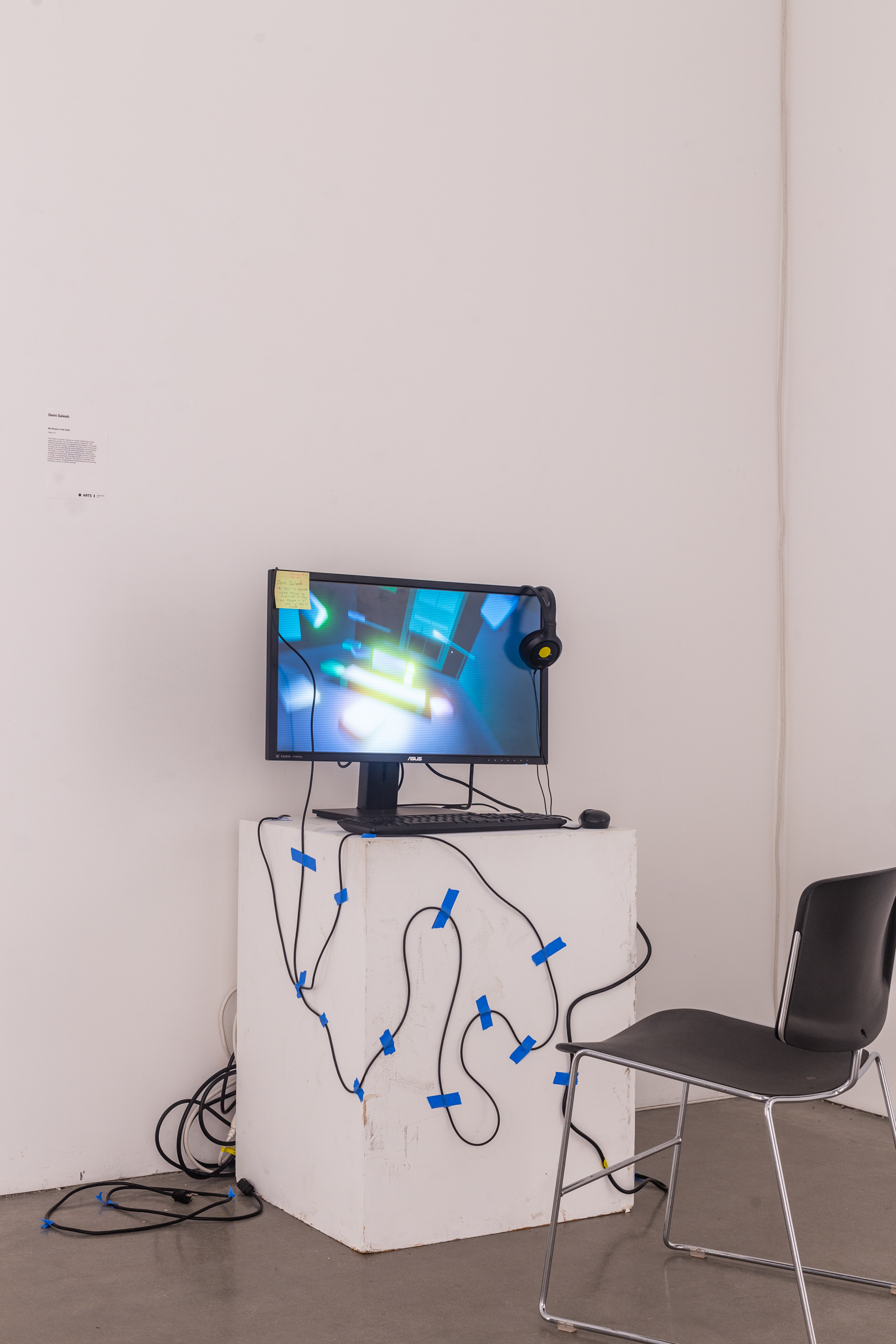 A white podium with a computer monitor, mouse, and keyboard with headphoens on the monitor. On the monitor is an interactive game.